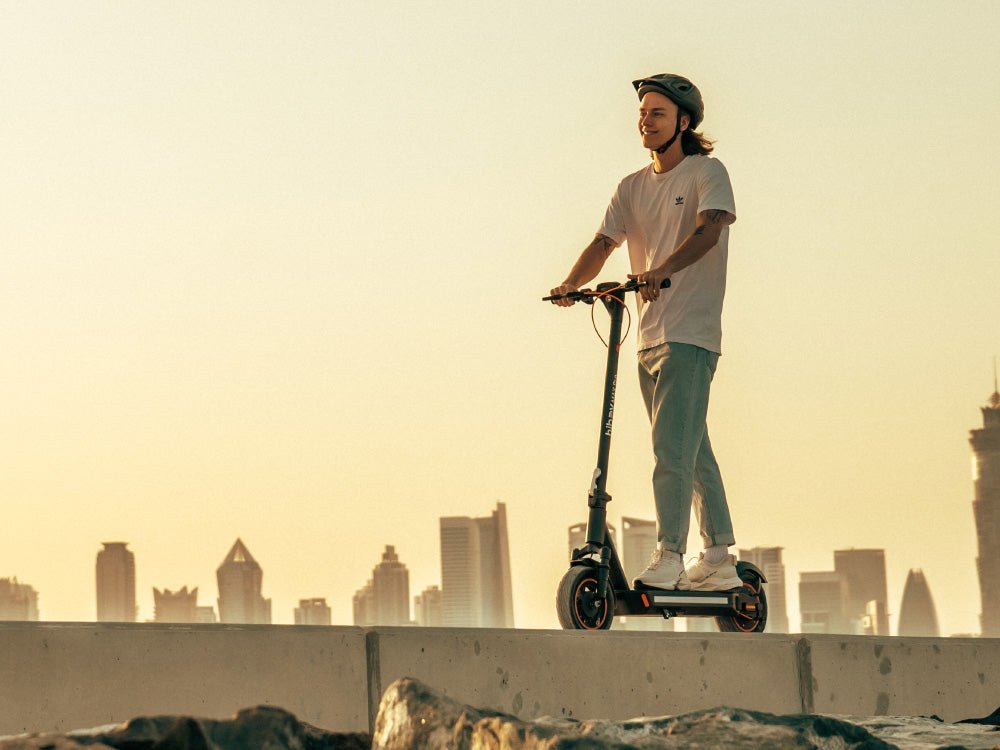 Rider on a Hiboy MAX Pro electric scooter on a wall at dusk with a city skyline behind