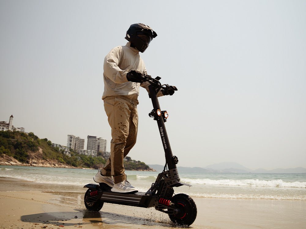 Rider on a Hiboy TITAN PRO electric scooter on a coastal path with a city skyline behind