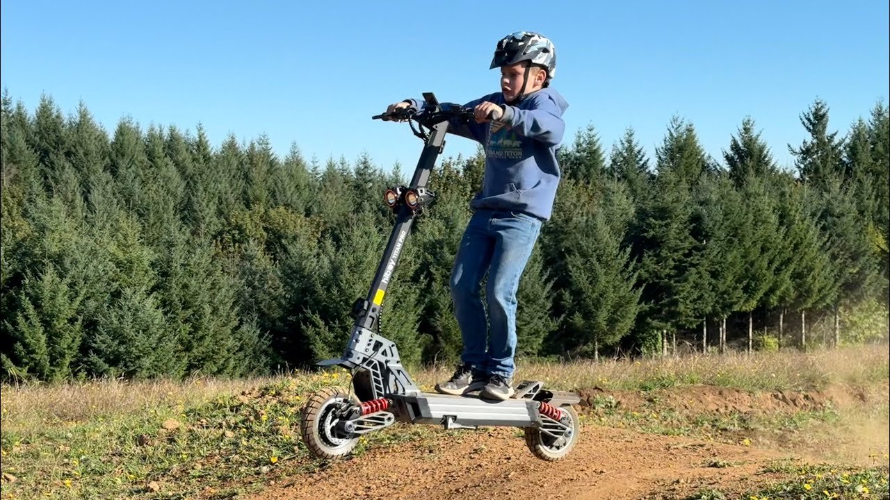 Adult rider standing on a Hiboy TITAN electric scooter on a grass track, showing the deck height against a full-height rider