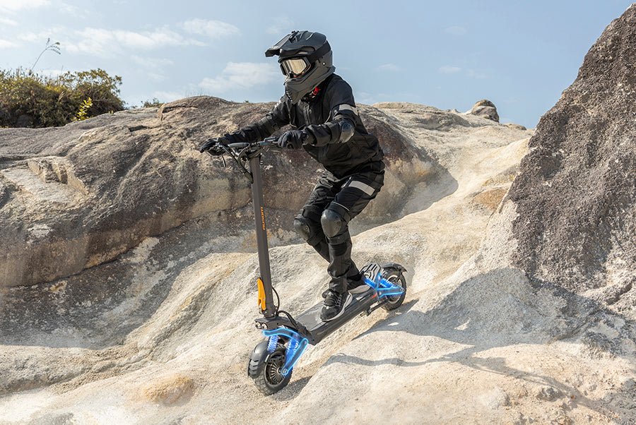 Rider descending a bare rock face on the Ausom F1 Max electric scooter with the suspension compressed