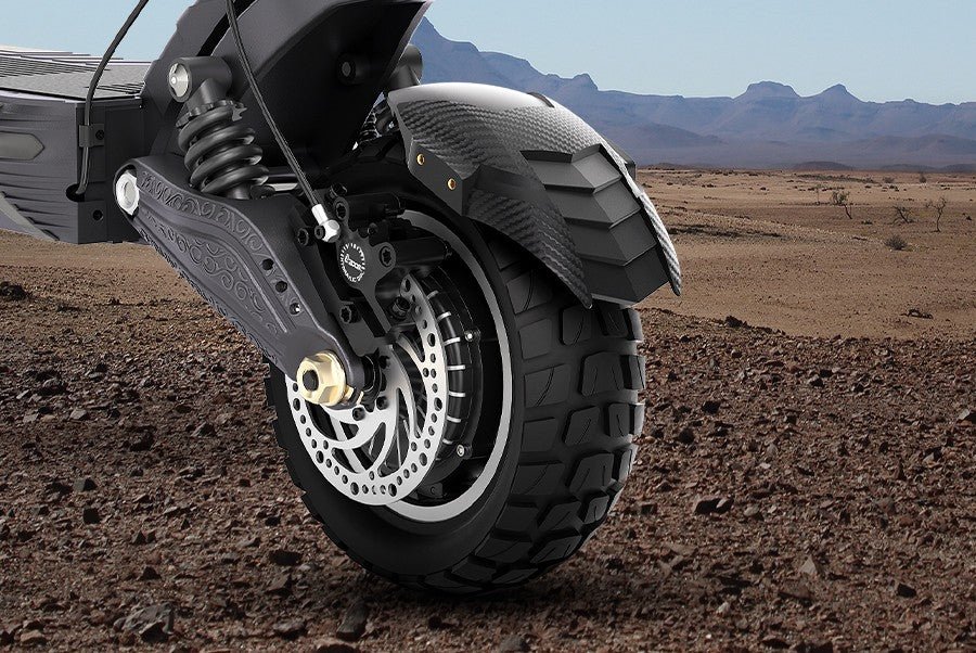 Front hydraulic disc brake and deep-tread tire of the Ausom F1 Max electric scooter against a desert backdrop