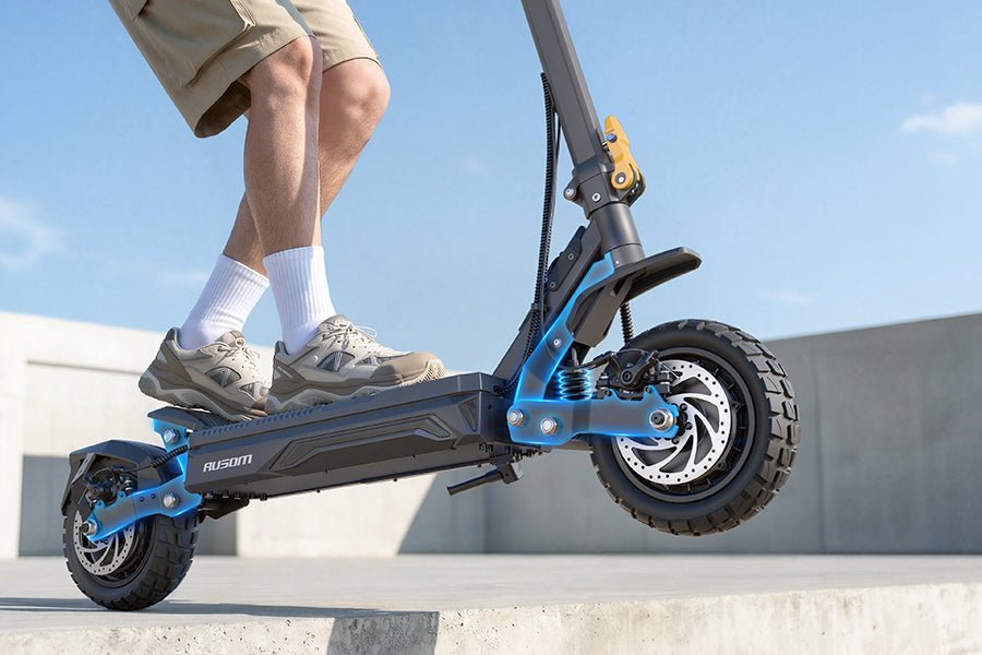 Rider standing on the Ausom Gosoul 2 Pro dual motor e-scooter showing the front swingarm suspension and off-road tire
