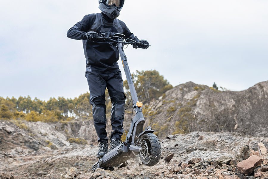 Rider in a helmet standing on the Ausom L2 Max electric scooter among rocks, showing the forged aluminum frame