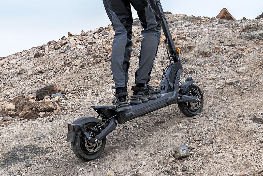 Rider climbing a rocky slope on the Ausom L2 Max electric scooter with its rear hub motor driving