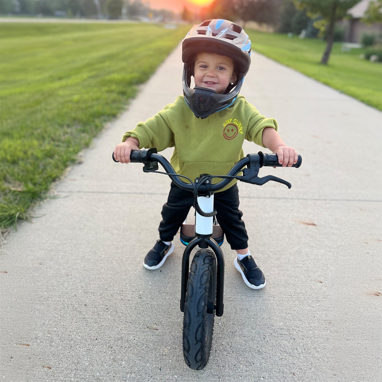 A young child riding a black Hiboy BK1 electric balance bike towards the camera along a paved path