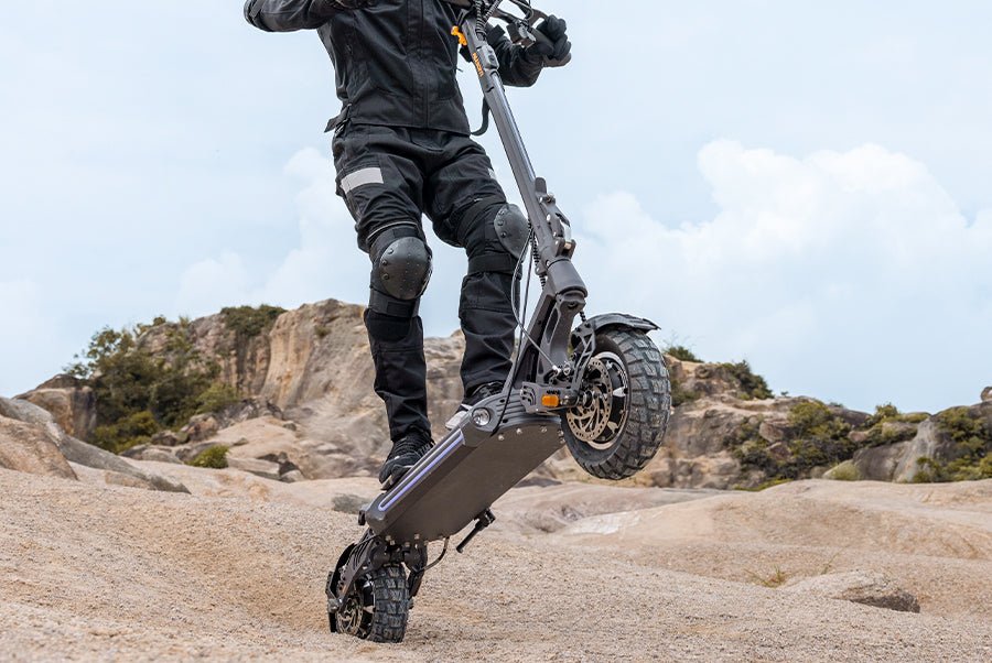 Rider pulling the front wheel of the Ausom SR1 electric scooter off the ground on a sandy rise