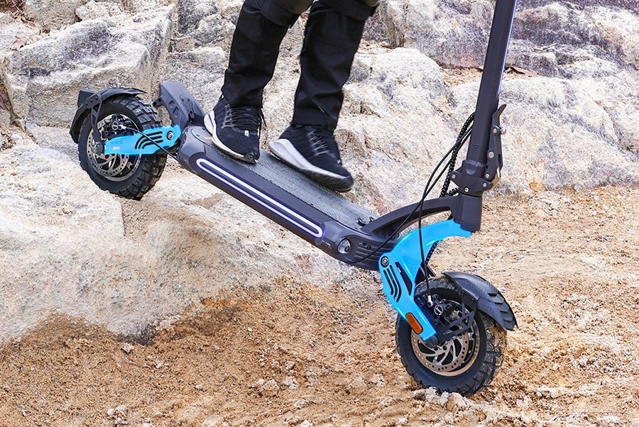 Ausom SR1 electric scooter cresting a rock ledge with both swingarms compressed under the rider