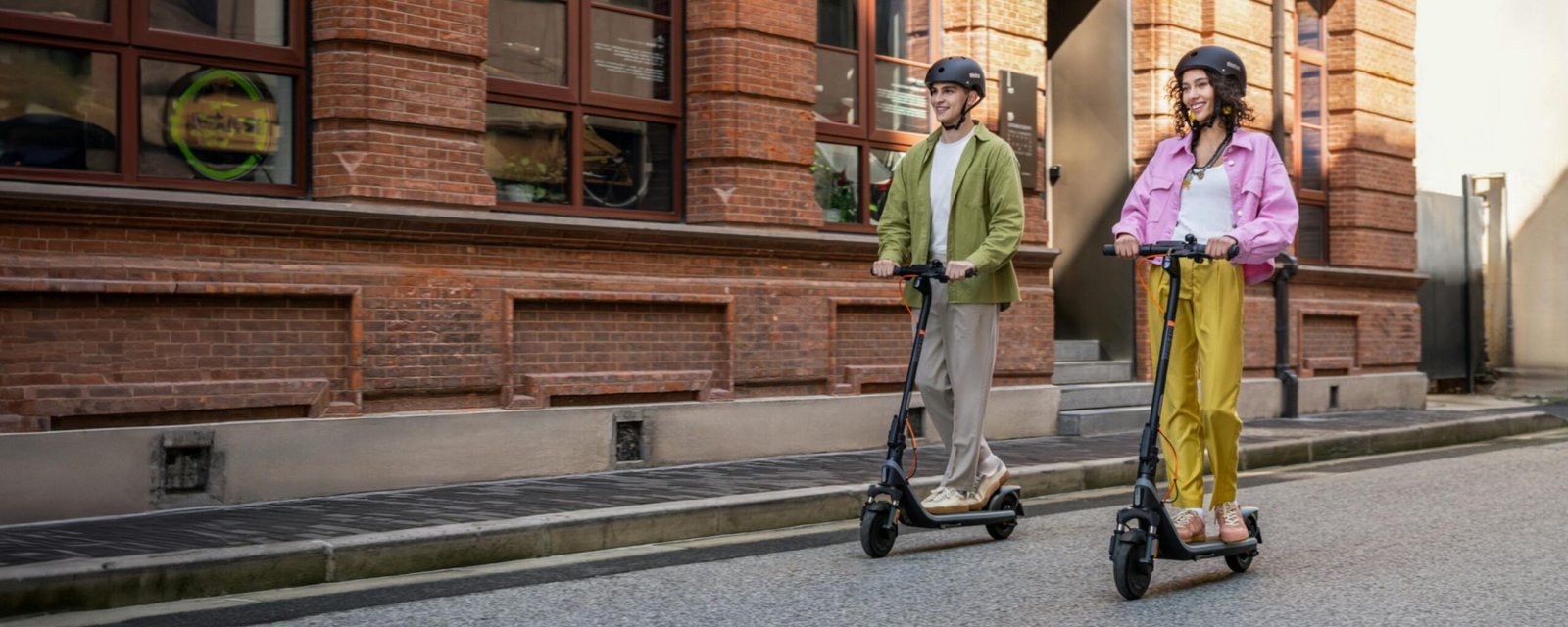 Two riders on Segway E2 Plus II electric scooters on a brick-lined city street