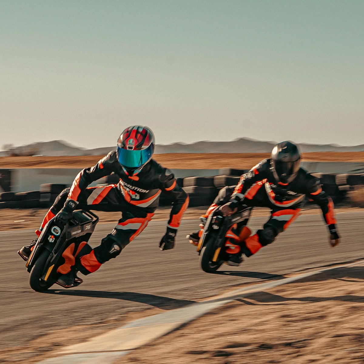 Two riders in leathers racing INMOTION P6 electric unicycles side by side on a track