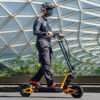 Rider on an INMOTION RS electric scooter beside a glass-panelled building