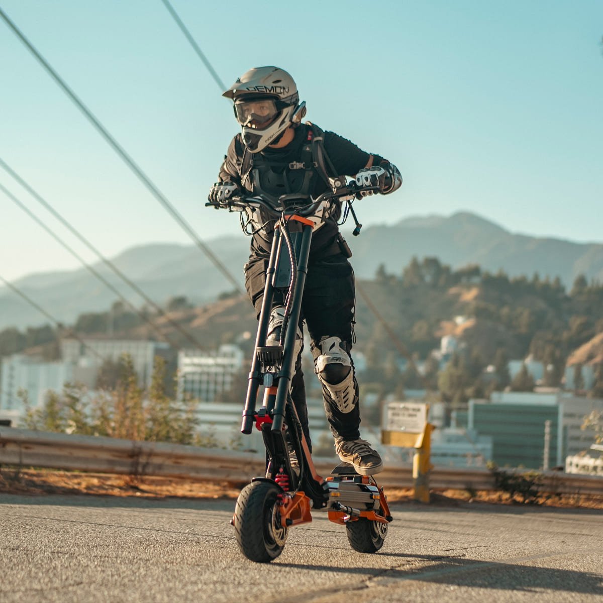 Rider on an INMOTION RS Lite electric scooter on a hillside road above a city
