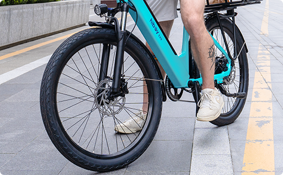 Front suspension fork and 26 by 2.5 inch tire of the teal Hiboy EX9 electric bike on a paved path