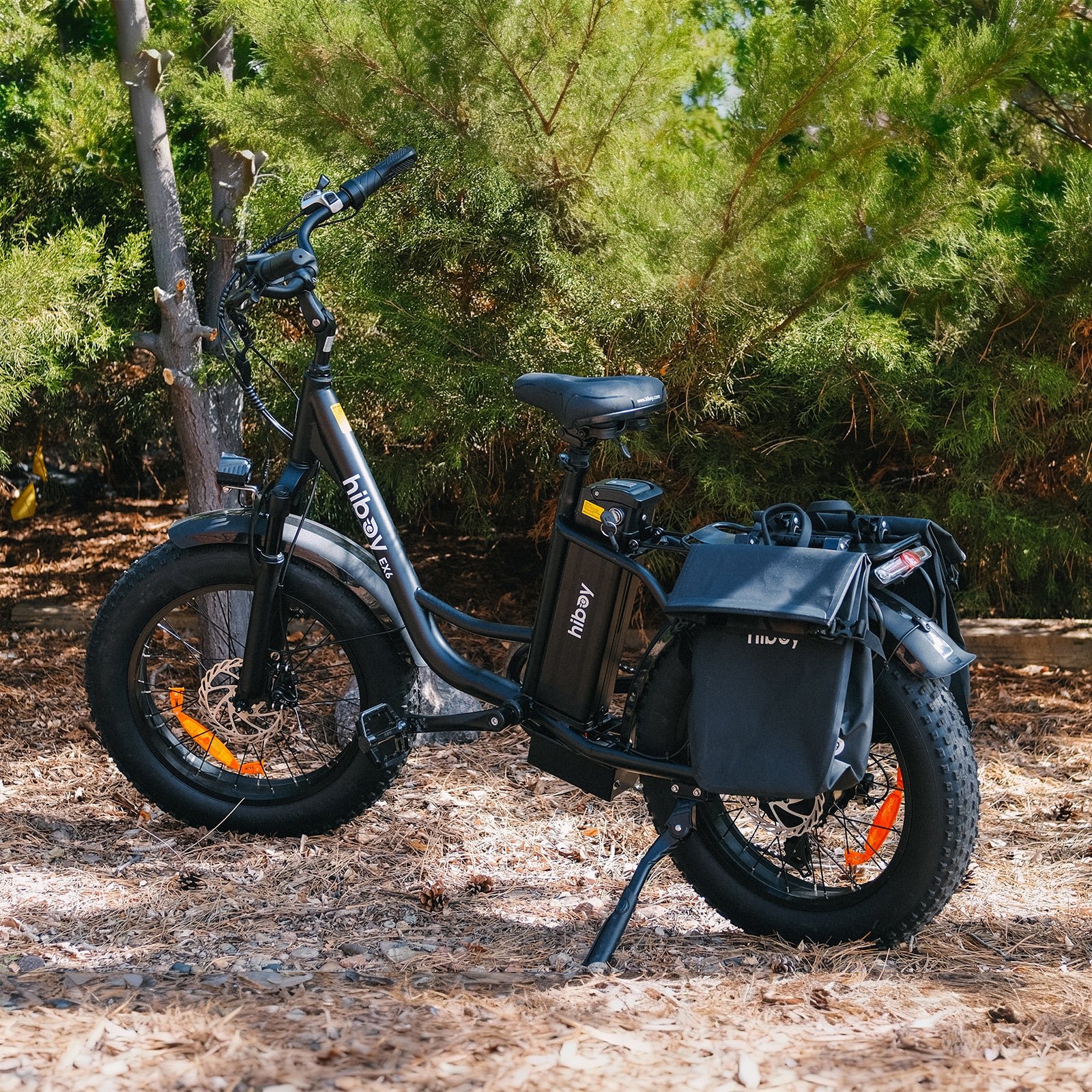 Black Hiboy EX6 electric bike with pannier bags parked under pine trees