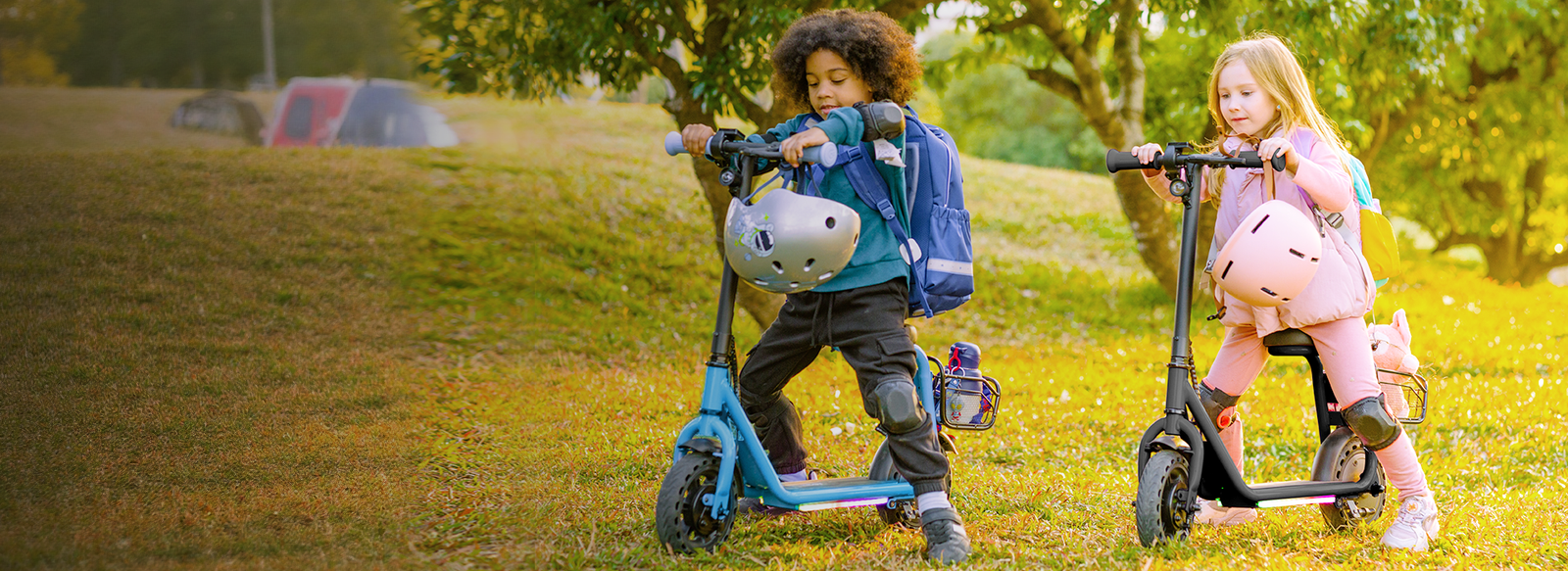 Two children with helmets and backpacks standing with blue and black Hiboy Q2 Lite kids electric scooters on a lawn