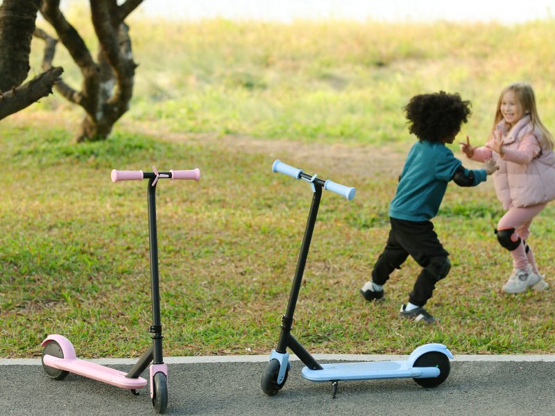 Pink and blue Hiboy ES1 kids electric scooters parked on a path while two children play on the grass