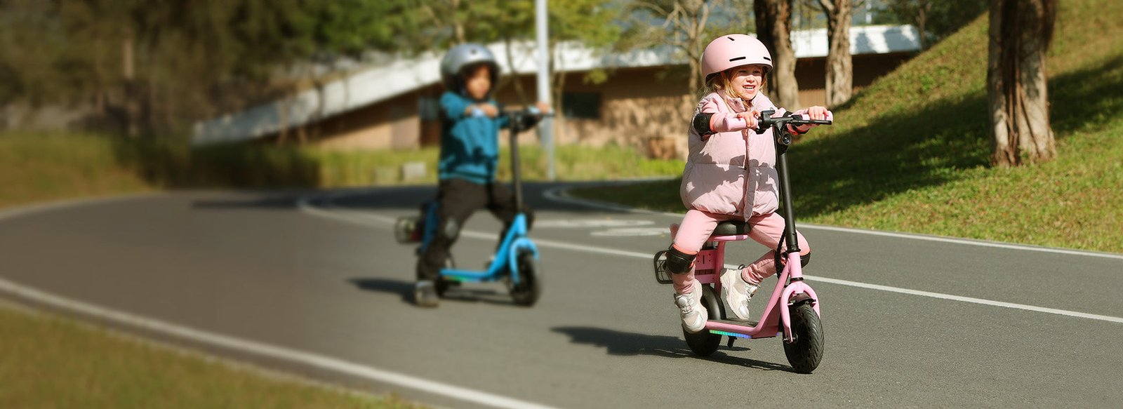 Child seated on a pink Hiboy Q2 Lite kids electric scooter riding along a path with another child behind