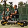 Two riders on the Teverun Blade Mini Ultra electric scooter beside a tennis court
