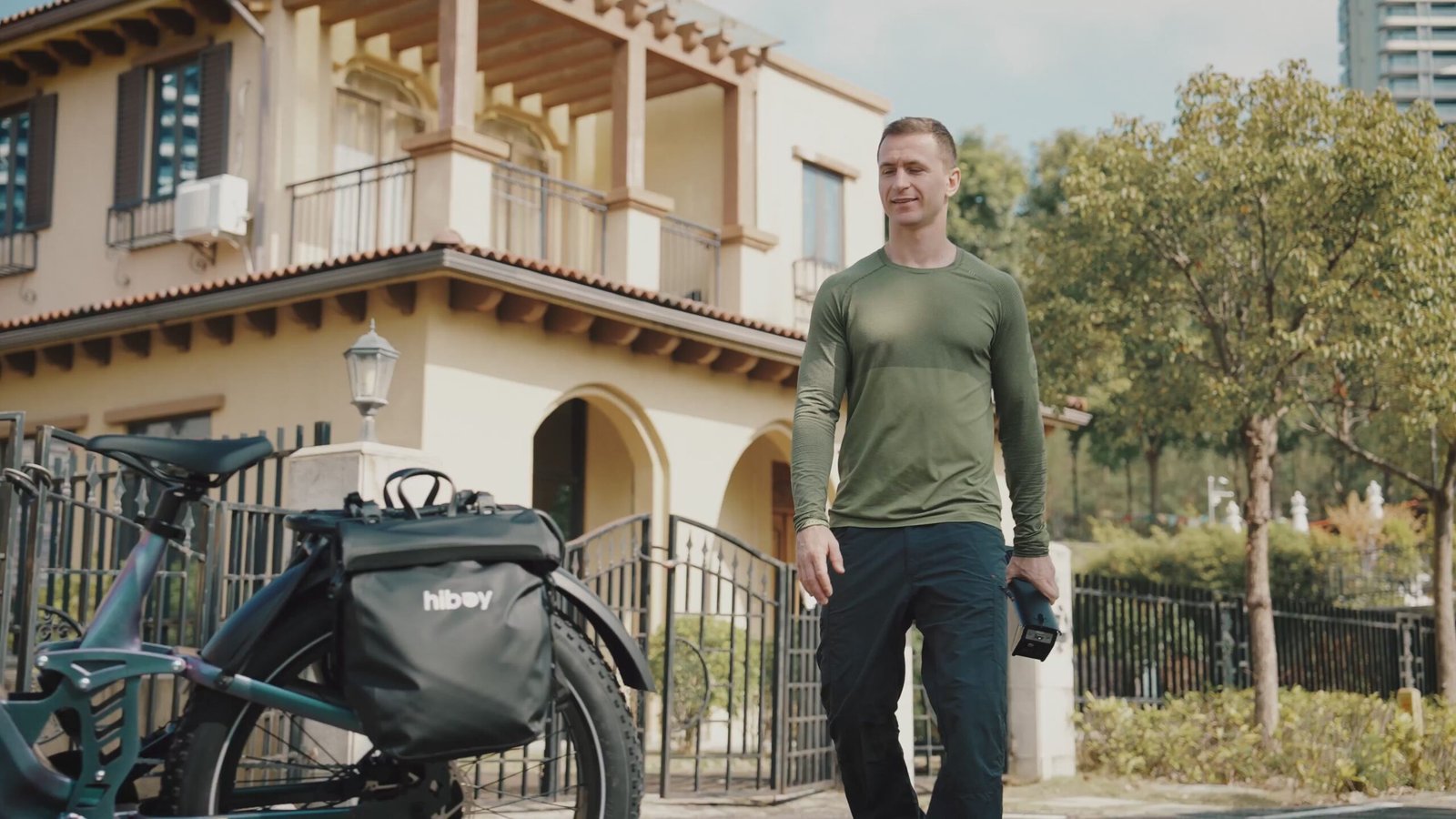 Rider carrying the removable battery away from a Hiboy EX11 full suspension electric bike fitted with pannier bags
