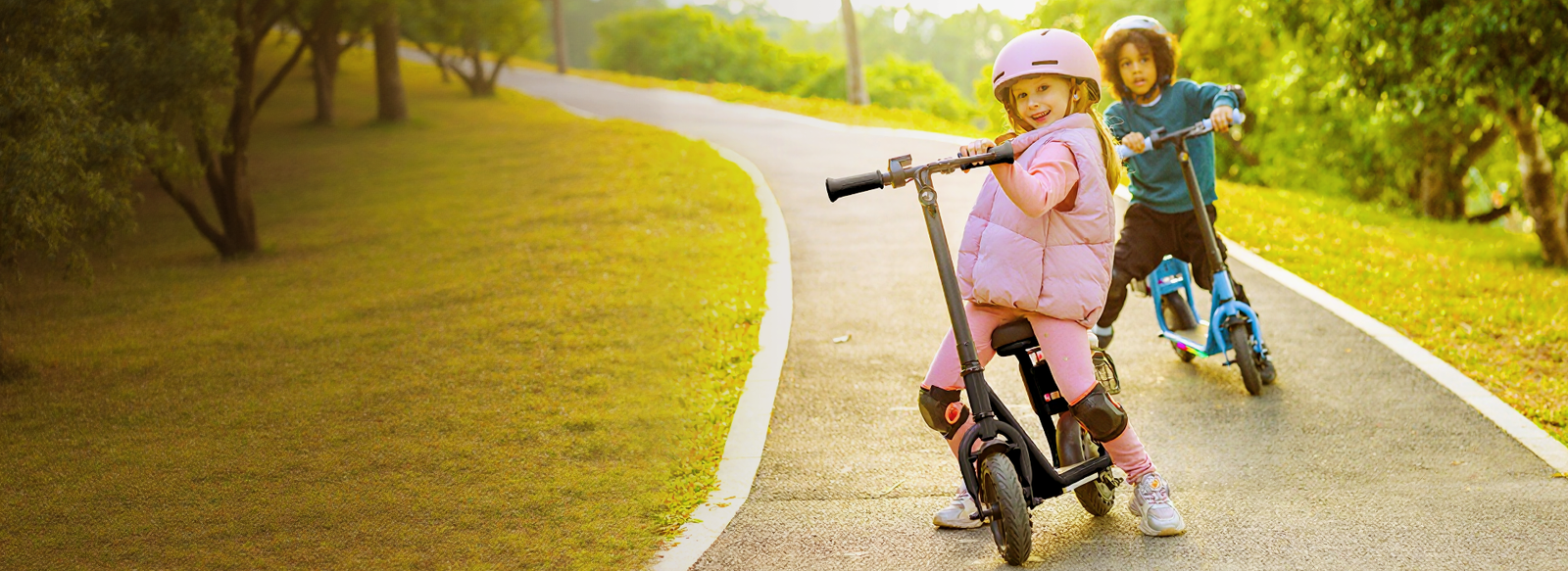 Two children in helmets on Hiboy Q2 Lite kids electric scooters on a sunny park path, one seated and one standing