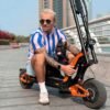 Rider sitting on an INMOTION RS Lite electric scooter on a waterfront promenade with a dog