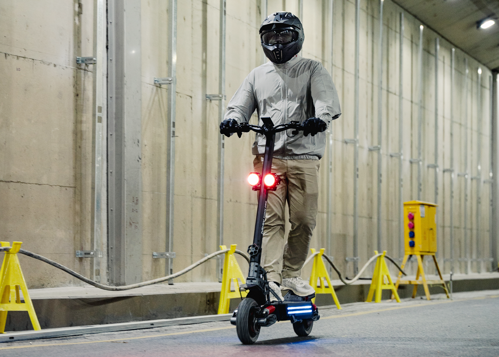Rider on the Hiboy TITAN electric scooter in a tunnel with twin headlights and blue deck lights on