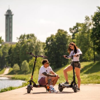 Two riders resting with the Teverun Blade GT II electric scooter by the river