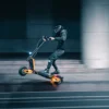 Rider on an INMOTION RS electric scooter at speed past a city building at night