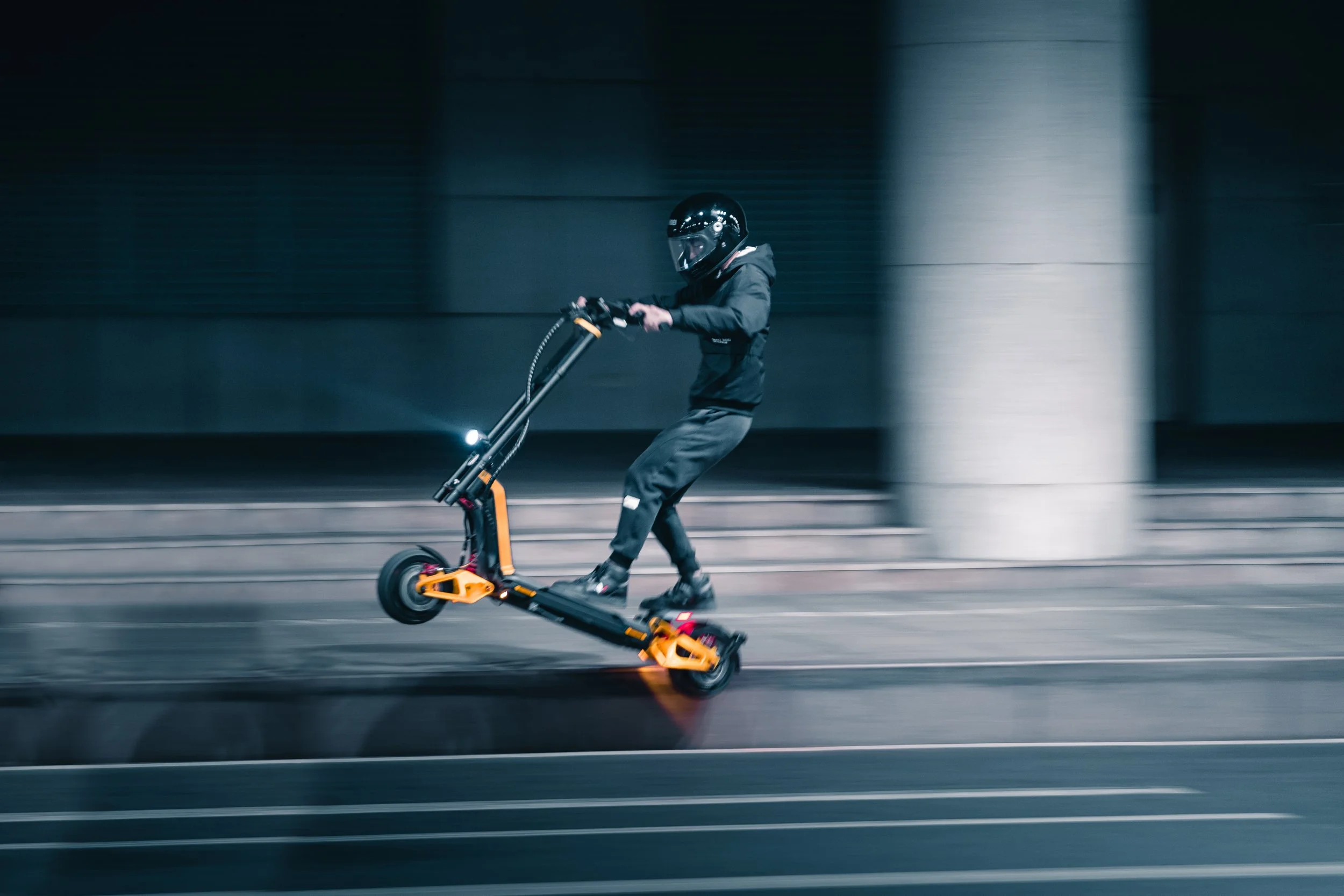 Rider on an INMOTION RS electric scooter at speed past a city building at night