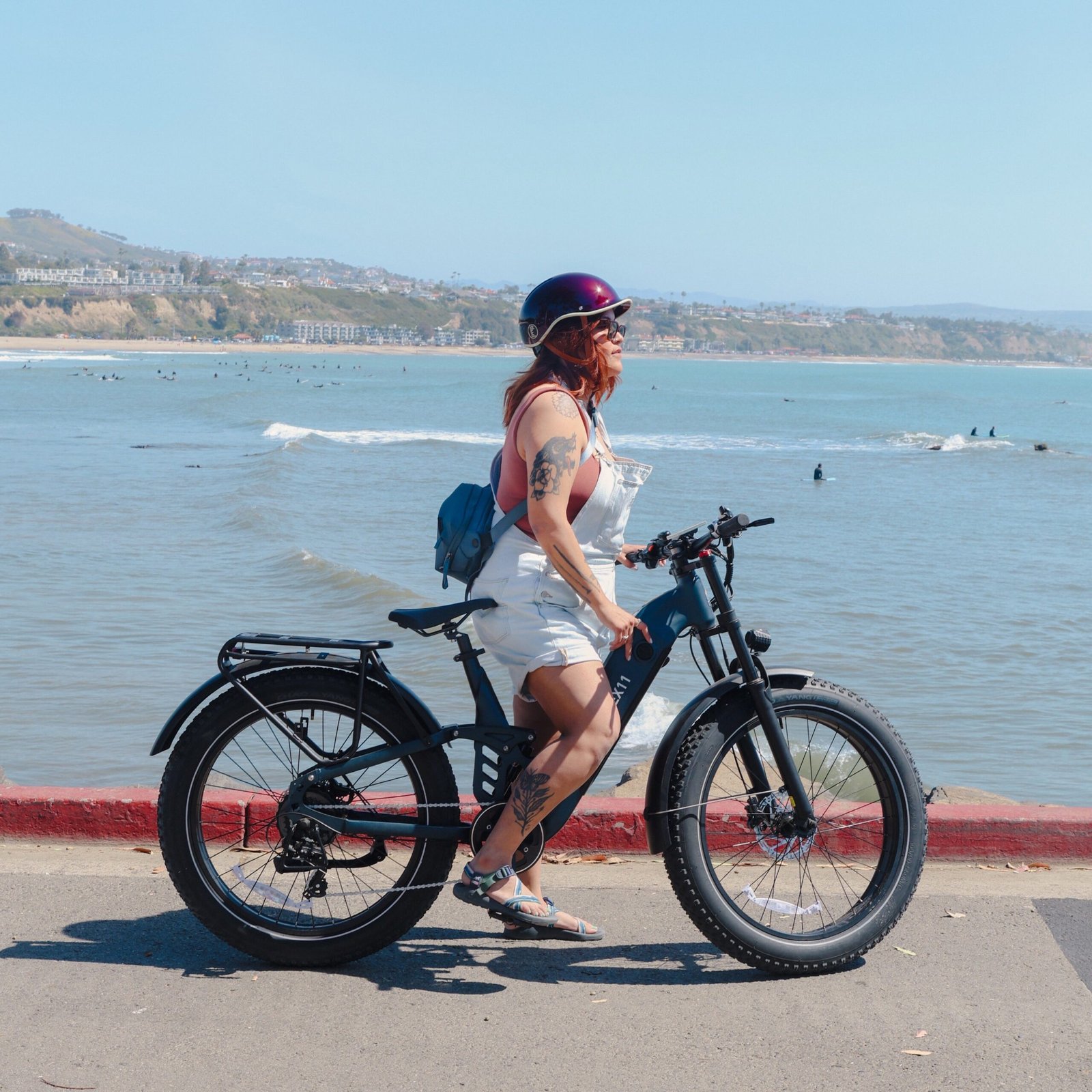 Rider in a helmet pausing on a navy Hiboy EX11 full suspension electric bike above a surf beach