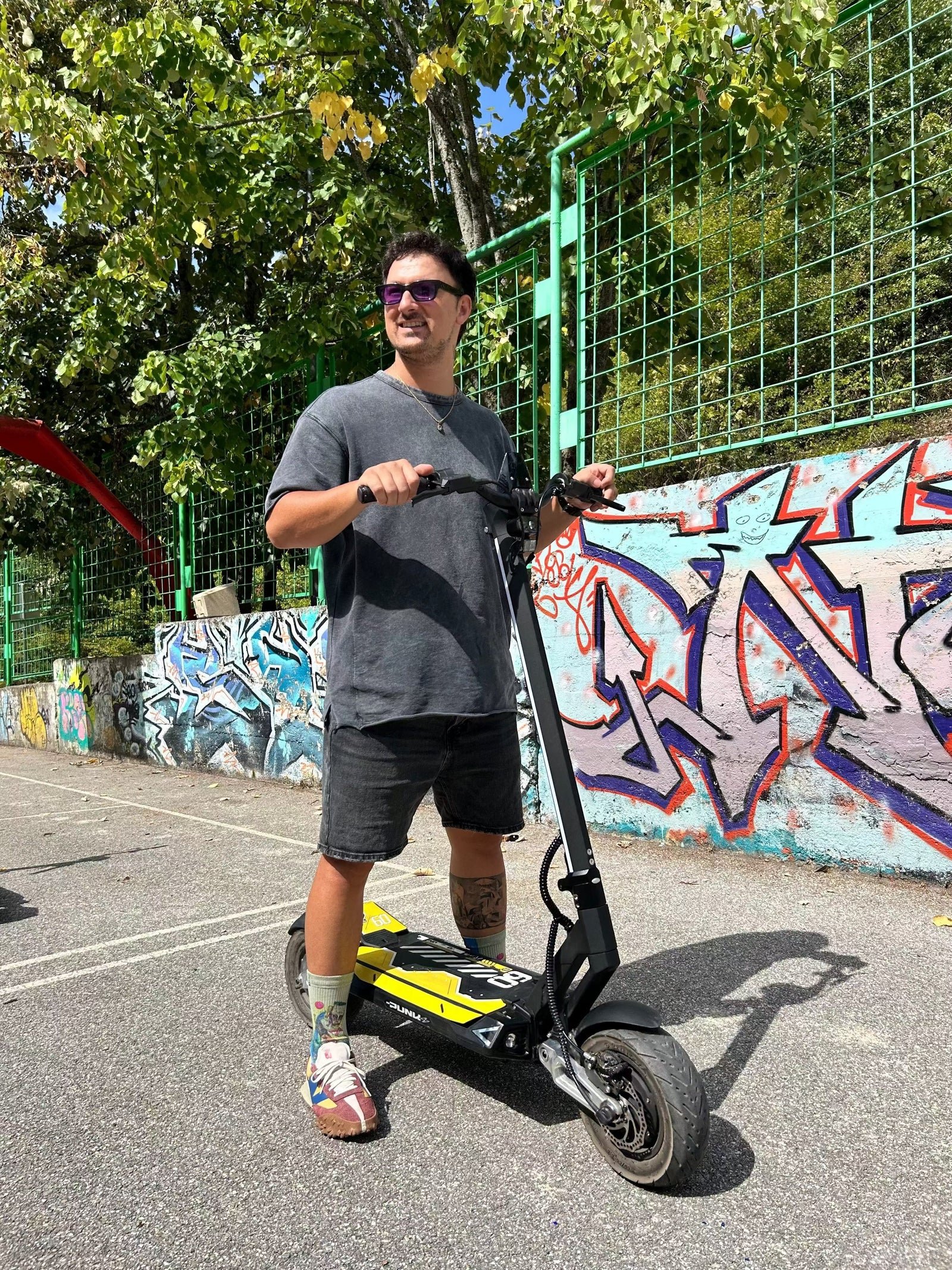 Rider standing over a Punk Rebel electric scooter beside a graffiti wall