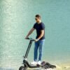 Rider on the Riding’times G63 Convertible electric scooter at the water's edge on a beach