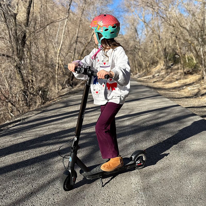 Child riding a black Hiboy S2 Lite electric scooter on a tree-lined road