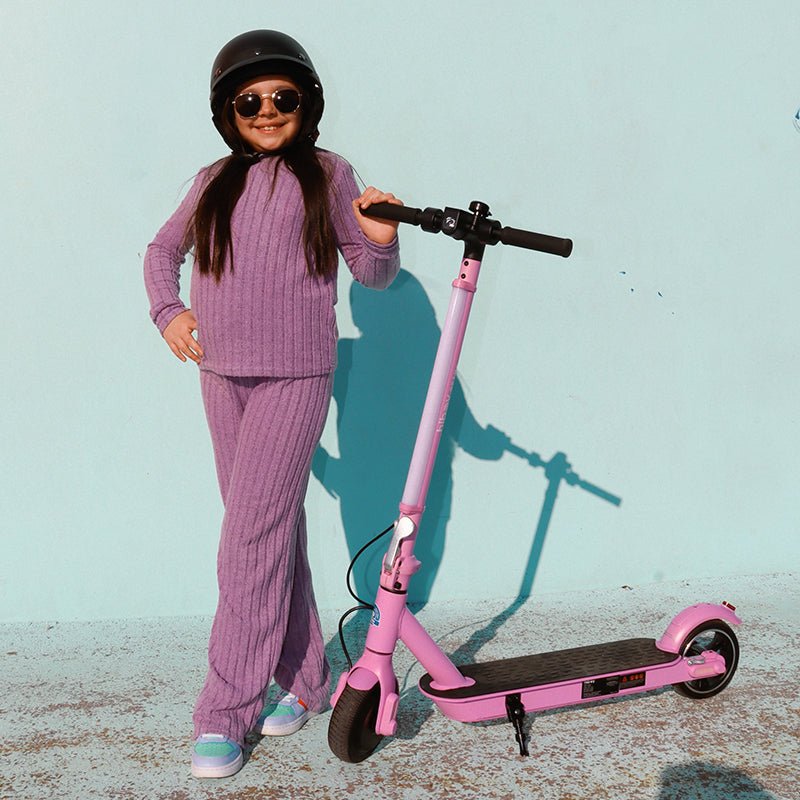 Child in a helmet standing beside a pink Hiboy S2 Lite electric scooter