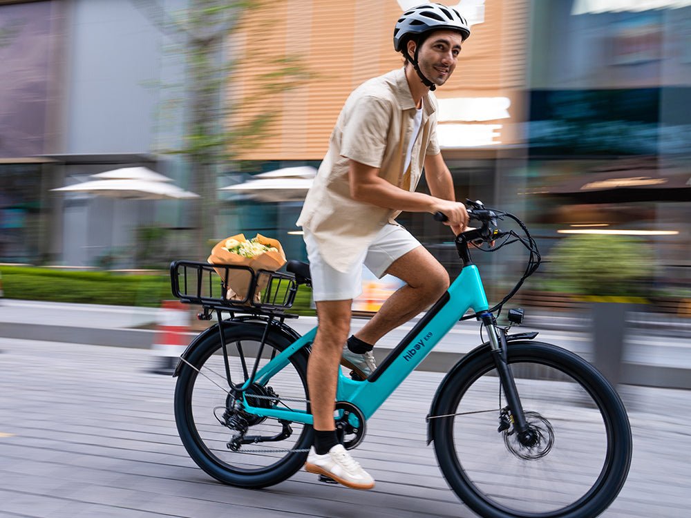 Rider on a teal Hiboy EX9 electric bike passing shopfronts with a bouquet in the rear rack