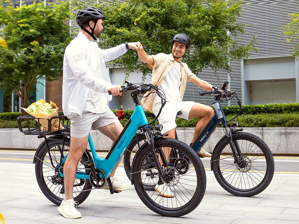 Two riders fist-bumping on teal and navy Hiboy EX9 electric bikes outside an office