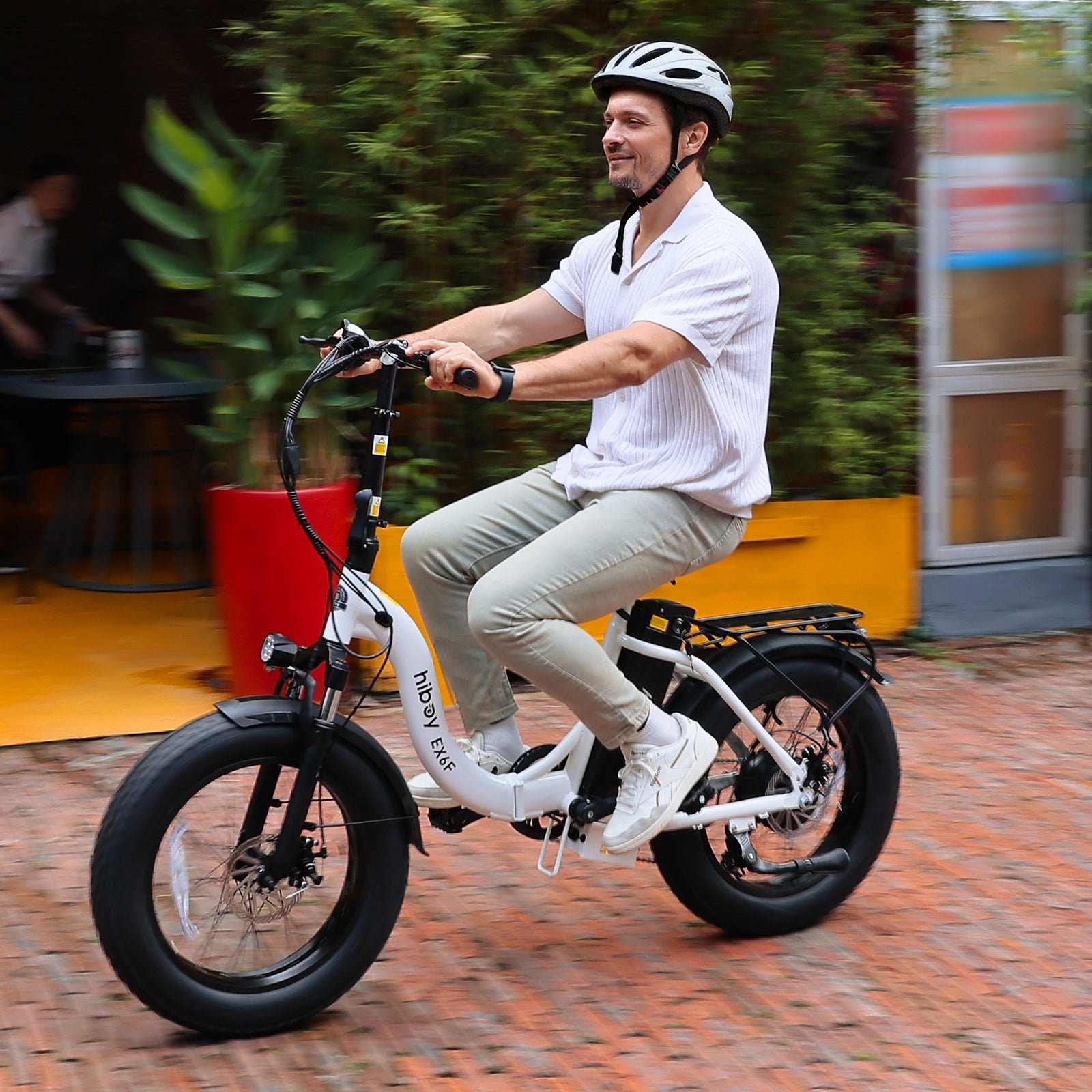 Rider on a white Hiboy EX6F folding electric bike passing a cafe