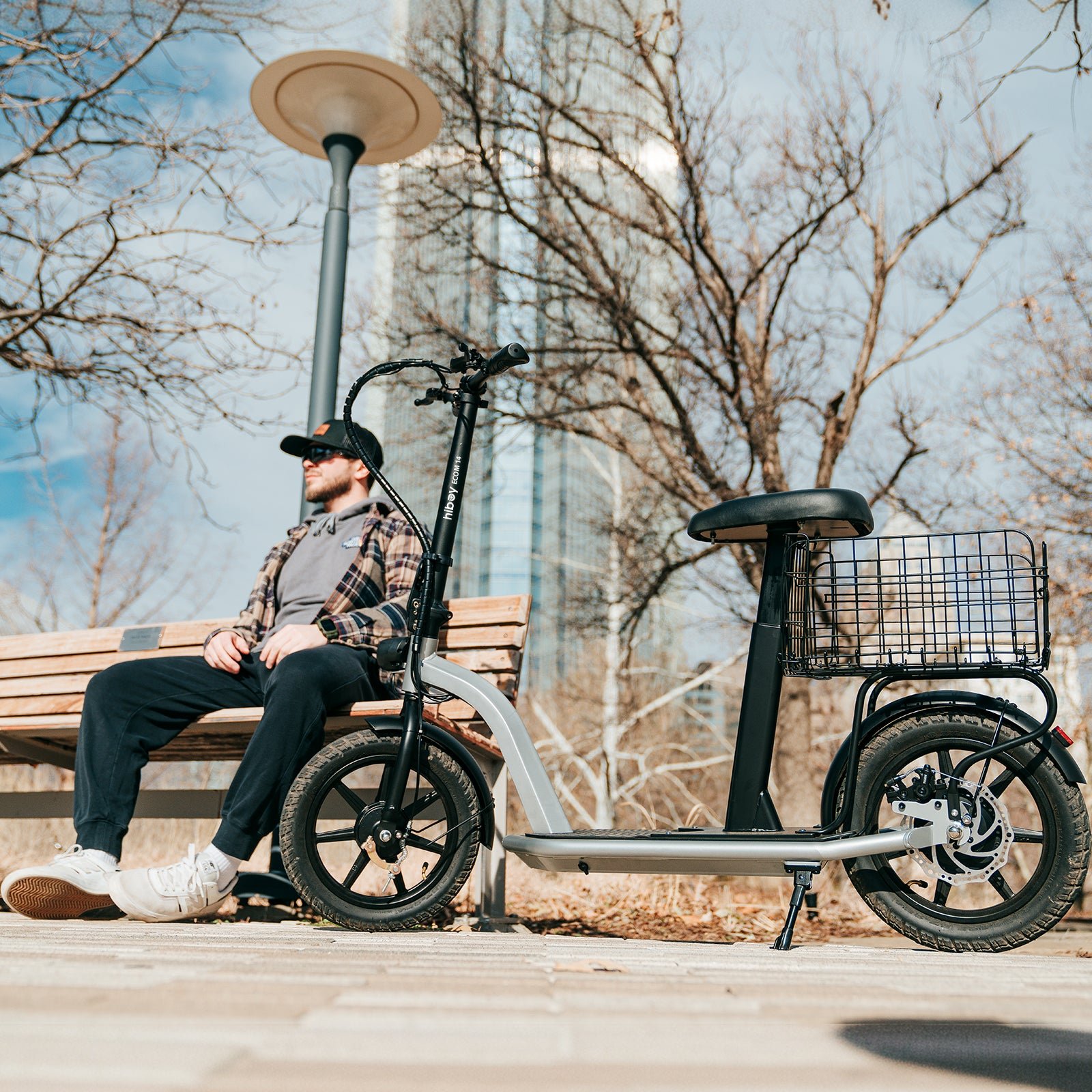 Hiboy ECOM 14 electric scooter with seat and rear basket parked beside a rider on a park bench