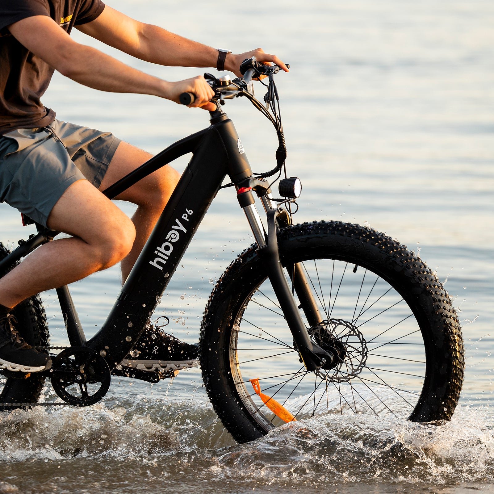 Rider on a Hiboy P6 fat tire electric bike splashing through shallow water at the shoreline