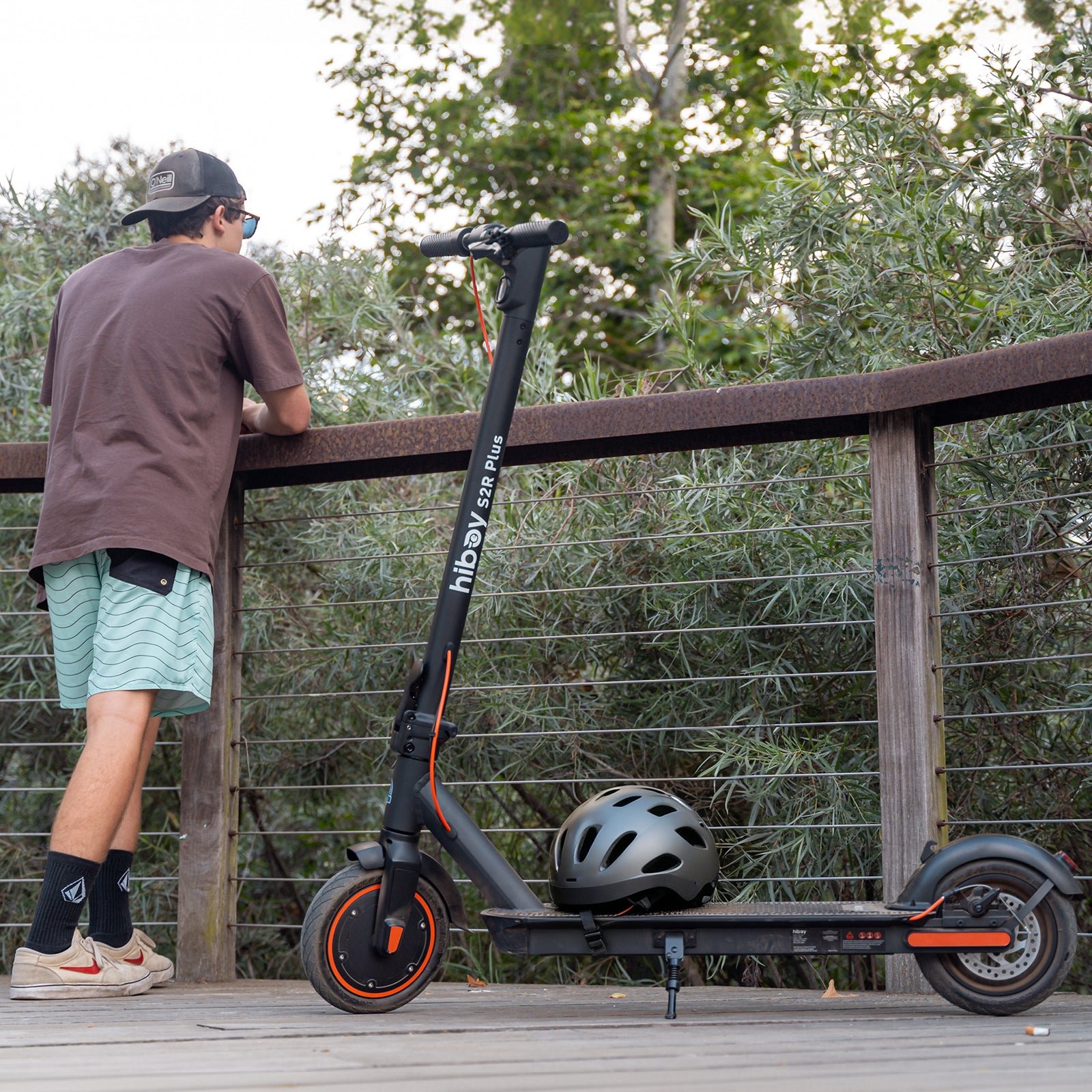 Hiboy S2R Plus electric scooter with a helmet on the deck at a boardwalk railing