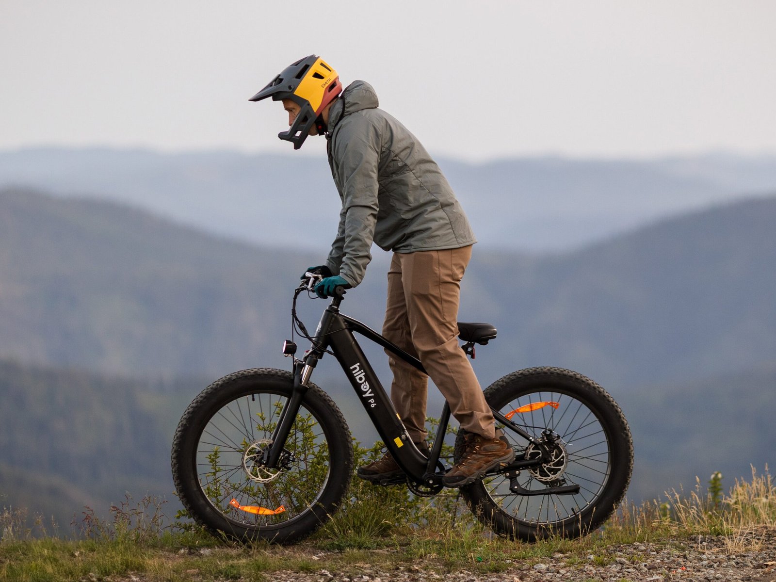 Rider in a full-face helmet standing over a Hiboy P6 fat tire electric bike on a mountain ridge