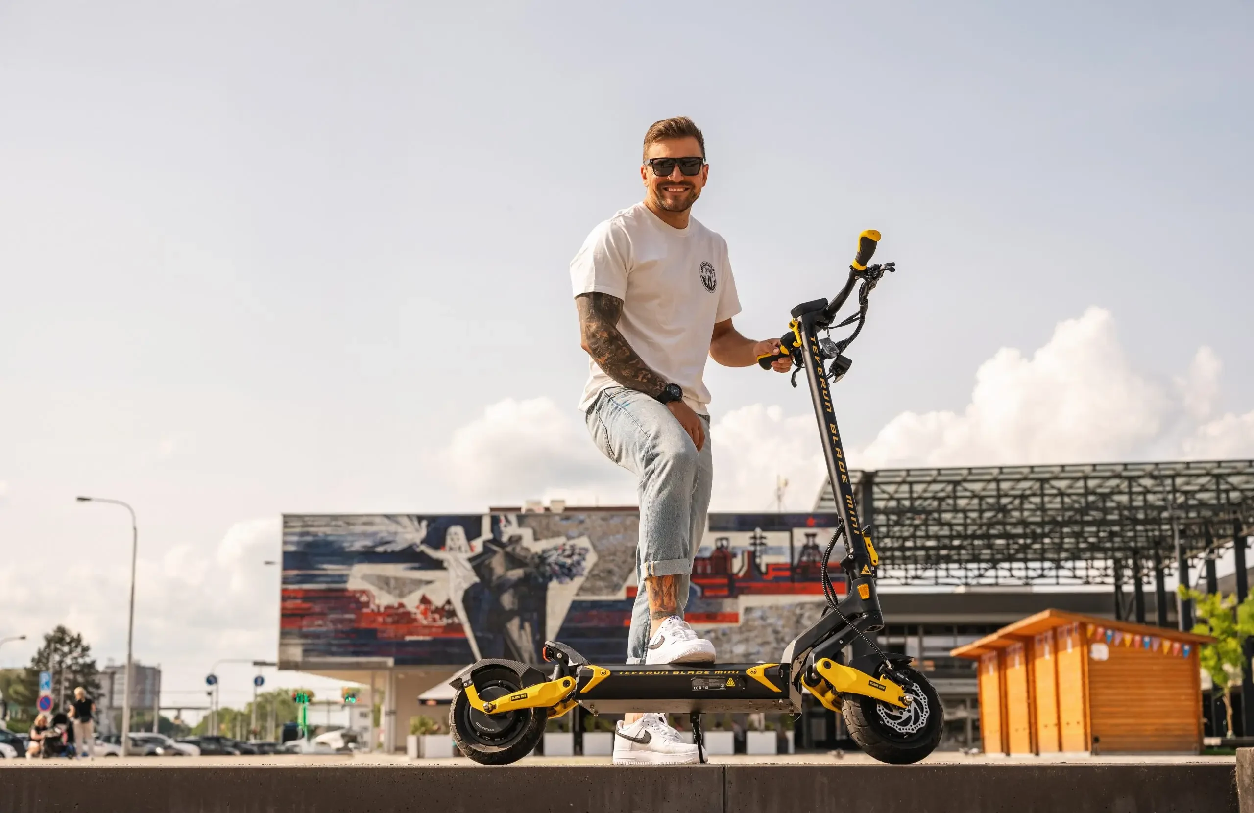 Rider pointing ahead beside the Teverun Blade Mini Ultra electric scooter on a sports court
