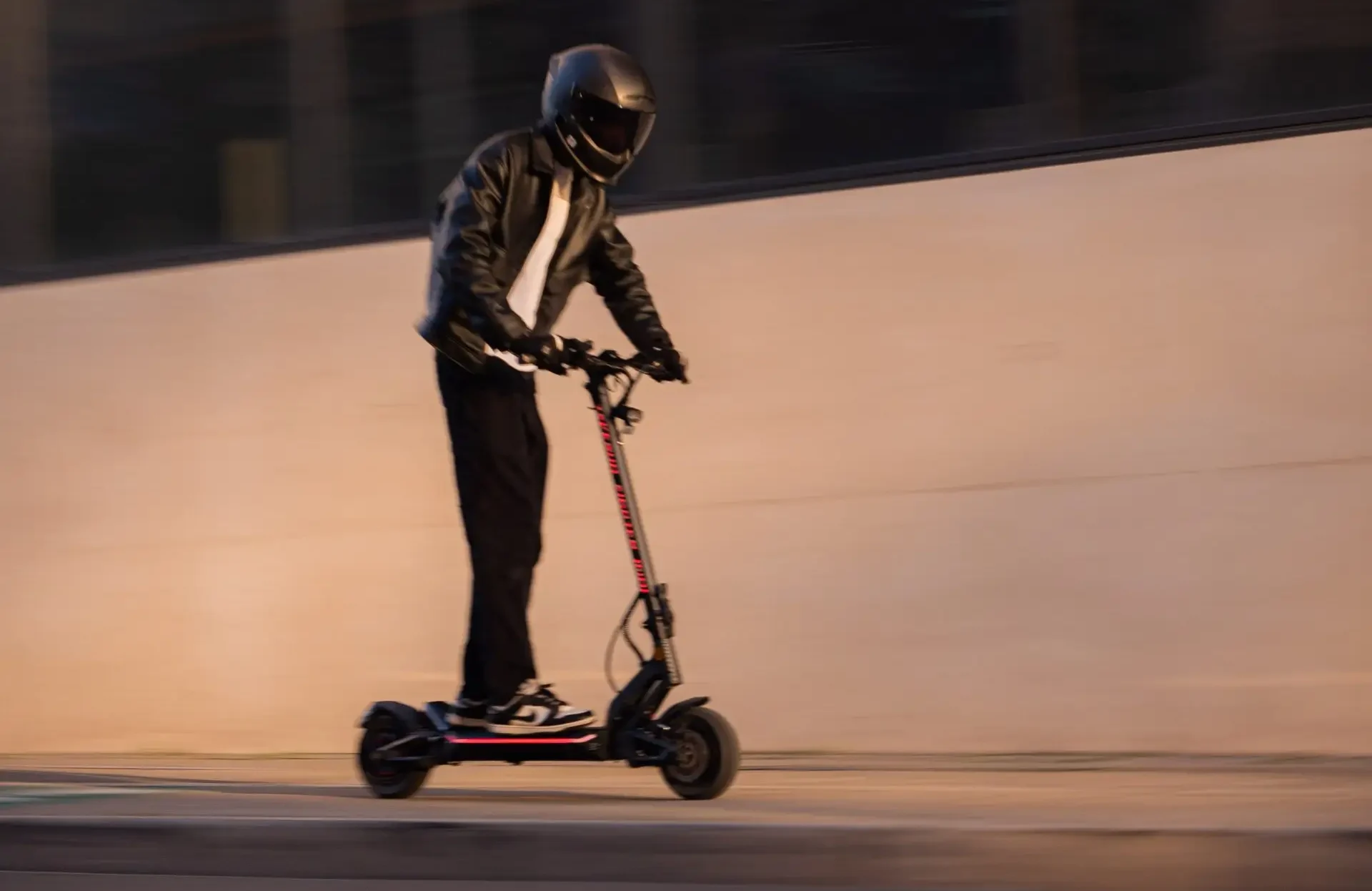 Rider on the Teverun Fighter Mini Pro electric scooter at dusk, riding past a concrete wall