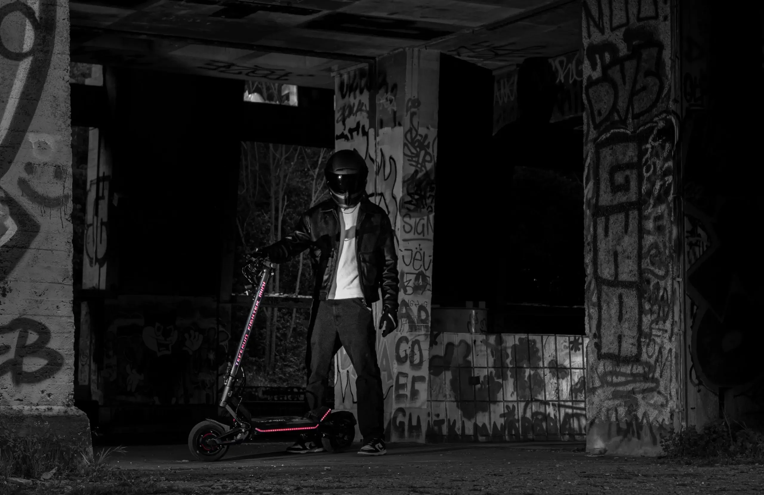 Rider with the Teverun Fighter Mini Pro electric scooter under a graffiti-covered bridge at night